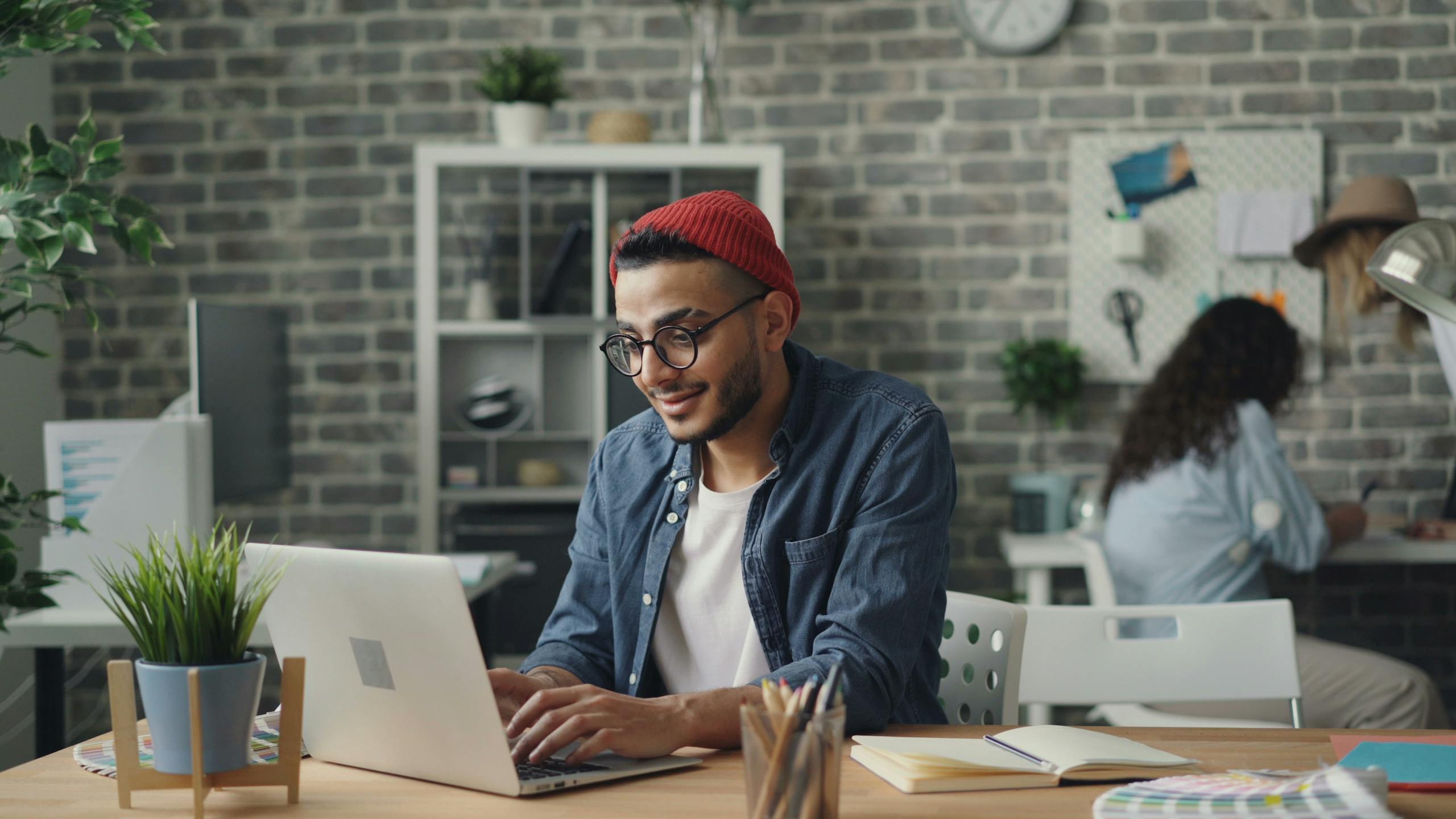 A young man in a beanie working diligently on a laptop in a stylish, modern office space.